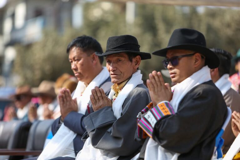 Three men in traditional attire with prayerful gestures at a cultural event.