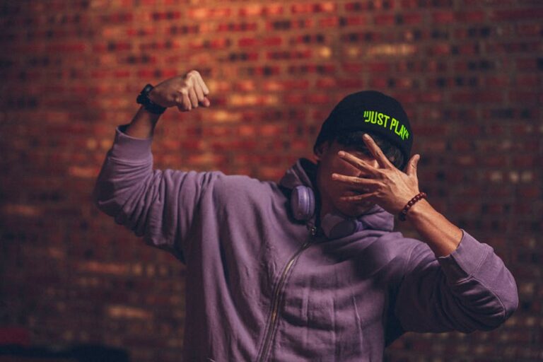 Hip urban fashion model posing with hoodie and cap, striking a dynamic pose against a brick wall.