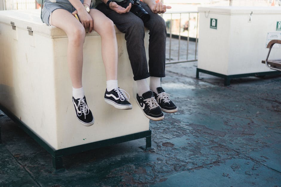 Two people sitting casually, showcasing their trendy sneakers against an urban backdrop.