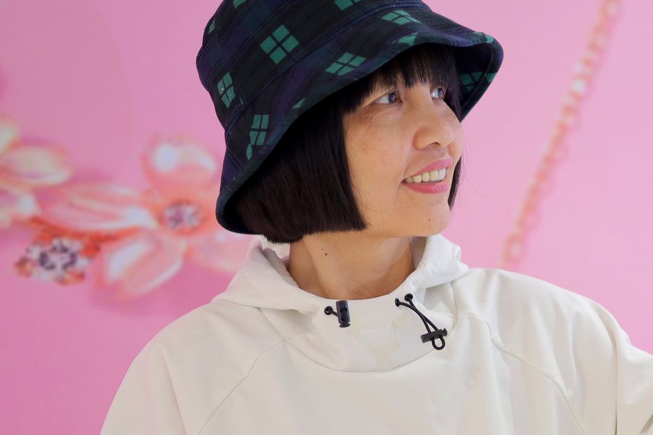 Woman smiling with a plaid bucket hat in front of a soft pink floral background.