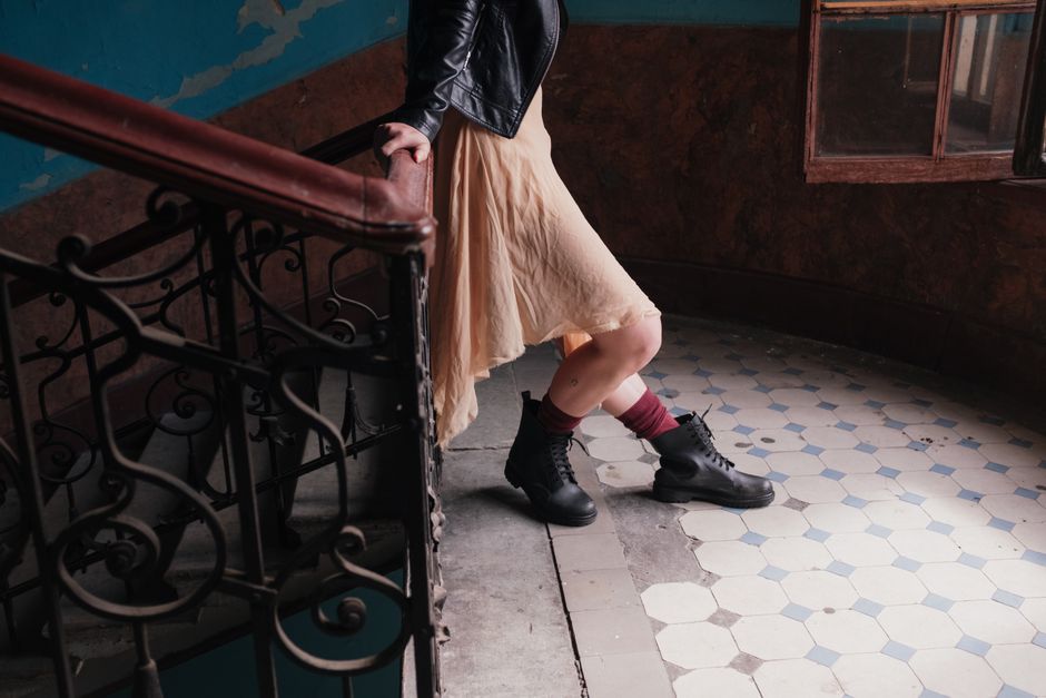Woman in boots and dress stands on antique staircase in old building.