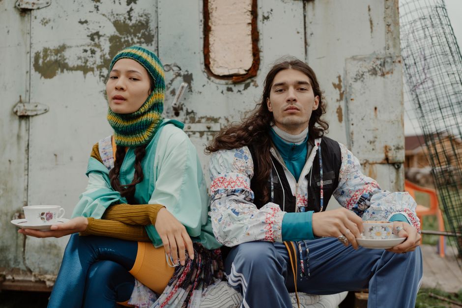 Stylish couple in eclectic outfits sitting outdoors and holding teacups.