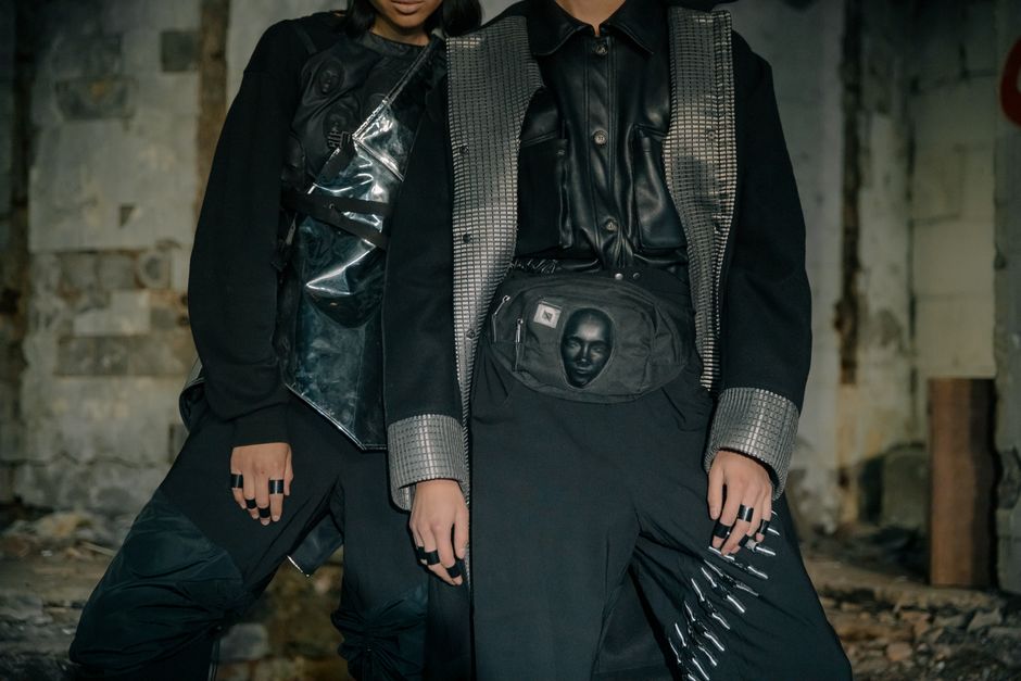 Two models in edgy cyberpunk attire pose in an industrial setting.