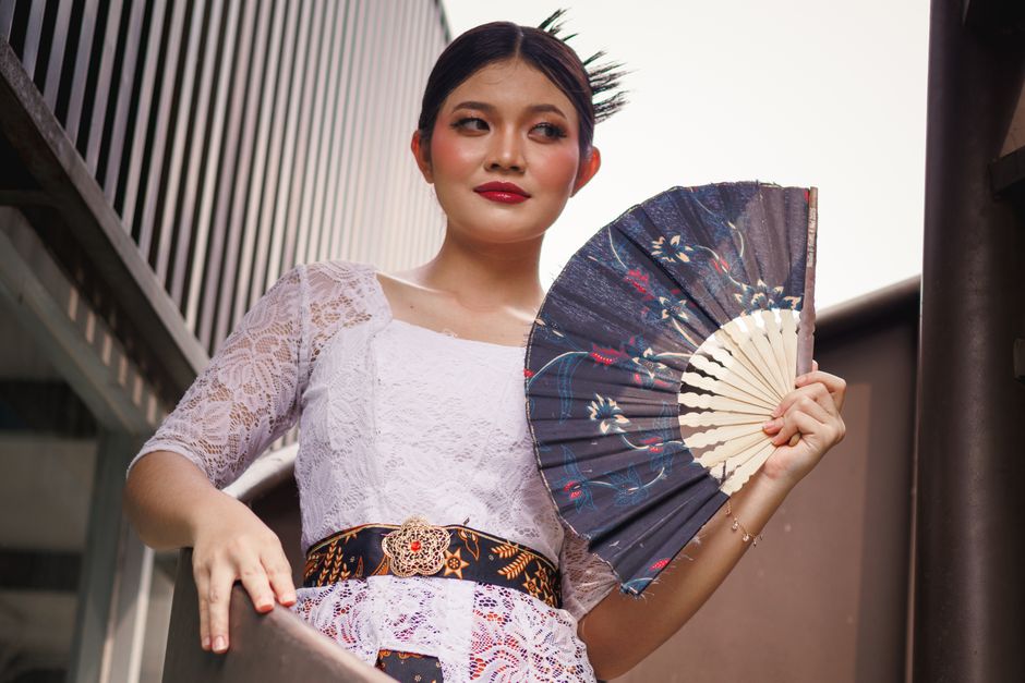 Stylish woman in traditional attire holding an ornate paper fan, showcasing cultural elegance.