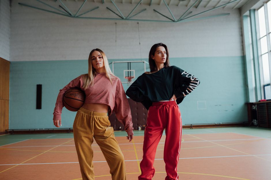 Two young women posing confidently on an indoor basketball court.