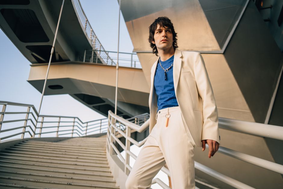 A fashionable man poses in a beige suit on a modern outdoor staircase, exuding confidence and style.