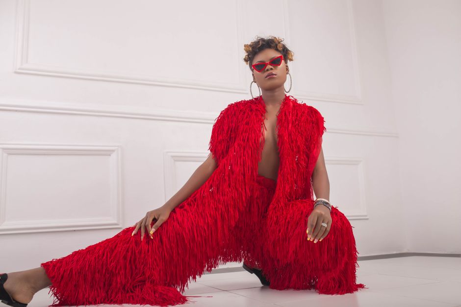 African American woman posing confidently in vibrant red fringed outfit and sunglasses.