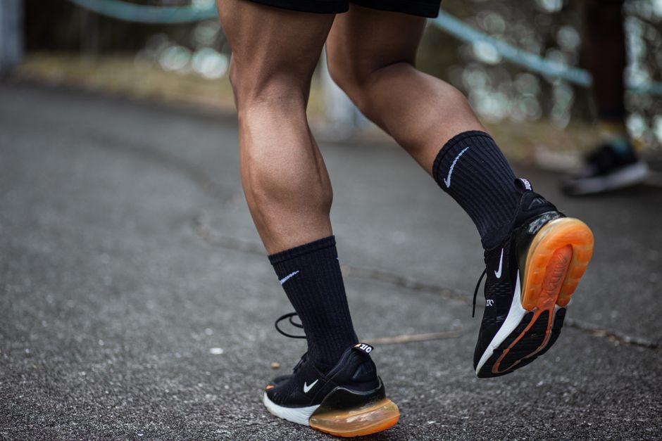 A close-up of a jogger's legs in motion on an asphalt road, emphasizing athletic footwear.