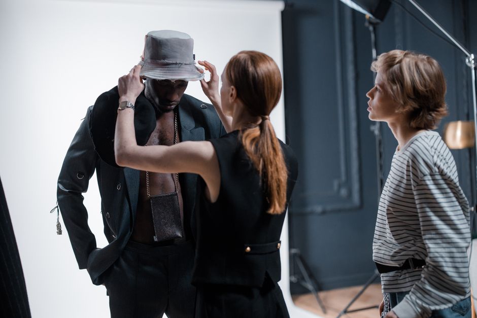 Fashion designers adjusting an outfit on a model during a studio photoshoot.