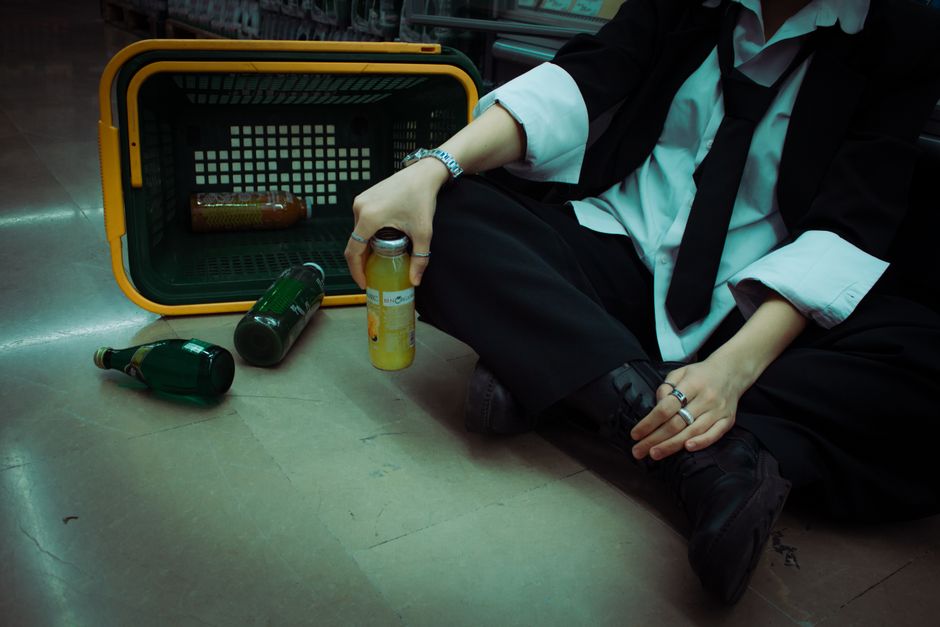 Person in formal attire sitting with grocery basket and bottles on the floor.