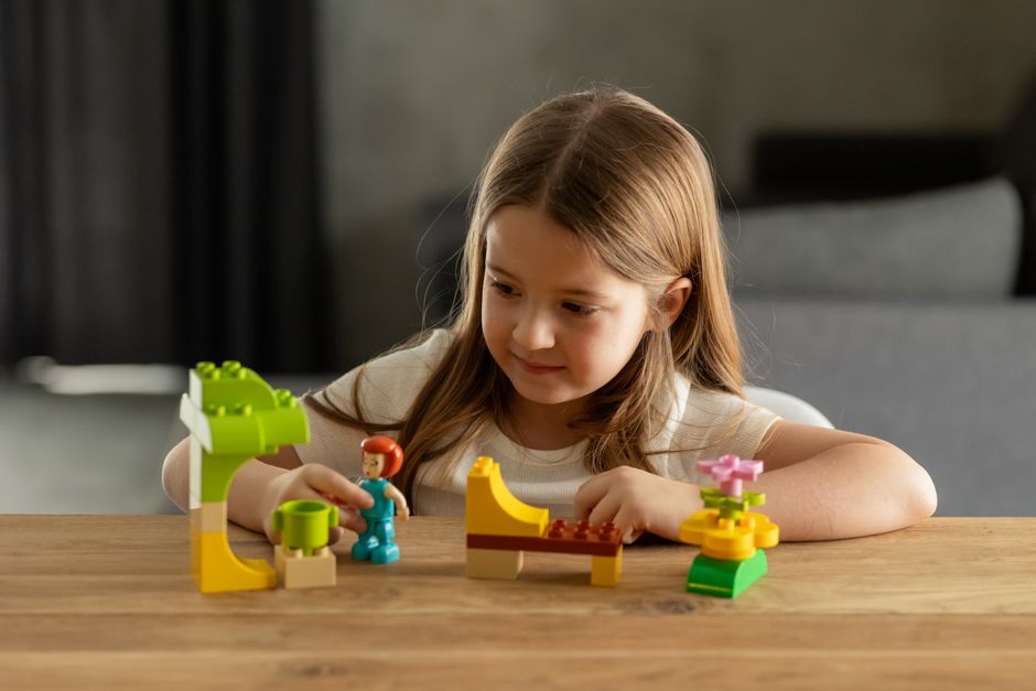 Girl building with colorful blocks on wooden table with focused expression indoors.