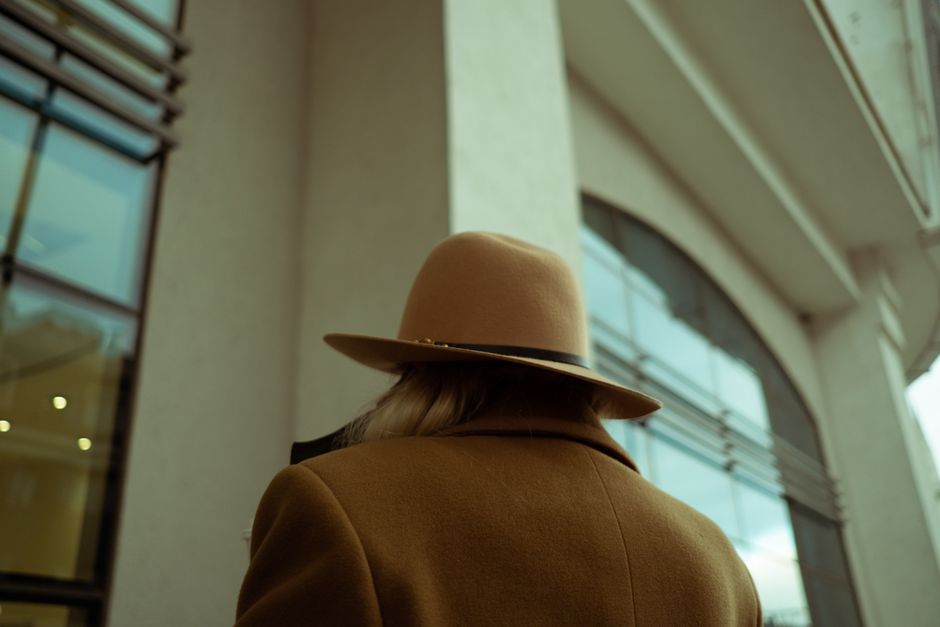 A woman in a wide-brimmed hat walks past a contemporary building.